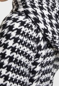 Tessuto a scacchi bianco e nero, texture morbida, con cappuccio e design aderente, enfatizzato da colori a contrasto.