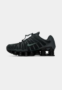 Crne i tamnosive Nike atletske cipele s jedinstvenim segmentiranim đonom i vezicama na povlačenje, prikazane na jednostavnoj bijeloj pozadini.
