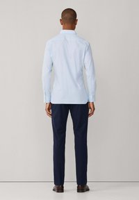 Svijetloplava košulja s dugim rukavima, nosi se uz tamnoplave hlače. Košulja ima klasičan ovratnik i ravni rub.