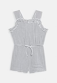 Jumpsuit a cuadros en blanco y negro con tirantes fruncidos, cinturilla elástica y detalle de lazo en el frente; tejido ligero y corto.