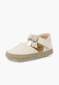 Zapato de espadrille beige con suela de yute trenzado, parte superior de lona y un lazo decorativo en la correa. Lados abiertos para ventilación.