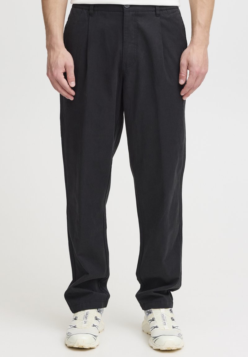 Pantalones negros plisados de algodón, con un corte recto y una cintura clásica, combinados con zapatillas blancas.