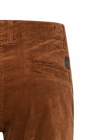 Bruine corduroy broek met verticale ribbels, een stevige tailleband en een achterzak met een patch. Subtiel logo detail aanwezig.
