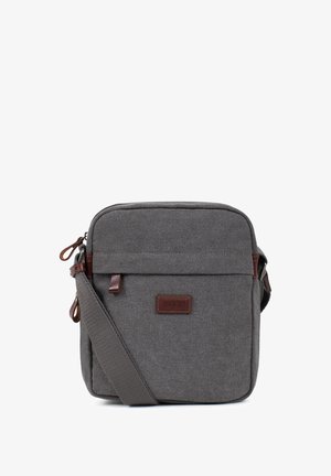 Sac bandoulière compact en toile grise avec sangle réglable, tirettes de fermeture éclair en cuir marron et écusson logo sur la poche avant.