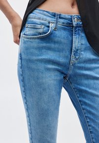 Μπλε τζιν παντελόνι με στενή εφαρμογή, σχεδιασμό πέντε τσεπών και εμφανείς ραφές. Το ύφασμα έχει υφή ξεθωριασμένου πλυσίματος.