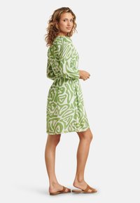 Groen en wit gestippelde jurk met lange mouwen, getailleerde taille, knie-lengte, gemaakt van gestructureerde stof. Draag het met bruine platte sandalen.