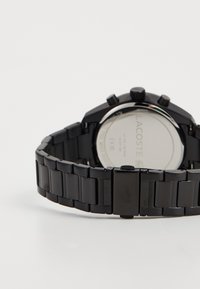Montre en acier inoxydable noir avec une surface lisse, des accents argentés, un boîtier rond et un bracelet à maillons. Présente un fond solide et rond.