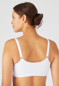 Sujetador blanco sin costuras con tirantes ajustables, textura suave y diseño minimalista. Presenta herrajes circulares en las uniones de los tirantes.