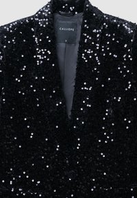 Blazer nero con paillettes, caratterizzato da un revers a lancia, chiusura con un solo bottone e superficie strutturata con paillettes scintillanti. Etichetta: CALLIOPE, taglia S.