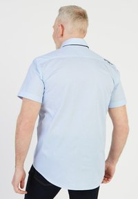Chemise légère bleu clair à manches courtes avec une texture à motif subtil, des poignets repliés et un col contrastant. Dispose d'une marque au dos.