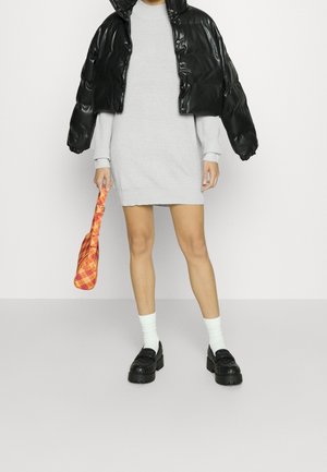 Giacca bomber nera cropped, vestito in maglia grigio, borsa a quadri arancione, calzini bianchi, scarpe nere con plateau. Texture liscia, design oversize.