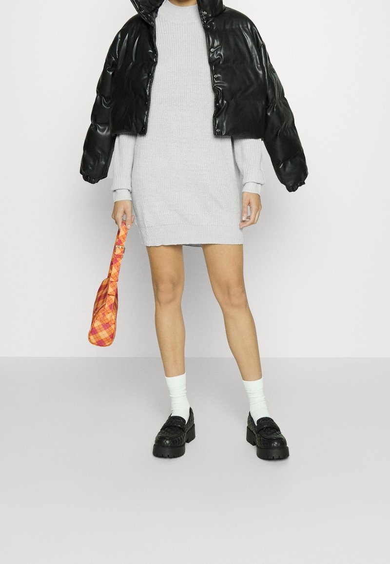 Svart kortad puffjacka, grå stickad klänning, orange rutig väska, vita strumpor, svarta plattformsskor. Slät textur, oversized design.