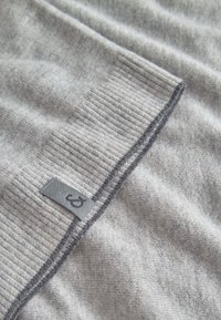 Grauer Strickpullover mit geripptem Kragen und strukturiertem Finish, versehen mit einem kleinen, in den Stoff genähten Markenetikett.