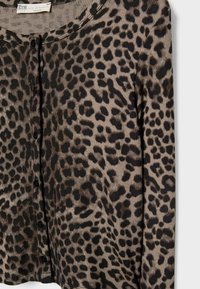 Camisa de manga larga abotonada con un patrón de print de leopardo en tonos marrones y negros, presentada sobre un fondo blanco.
