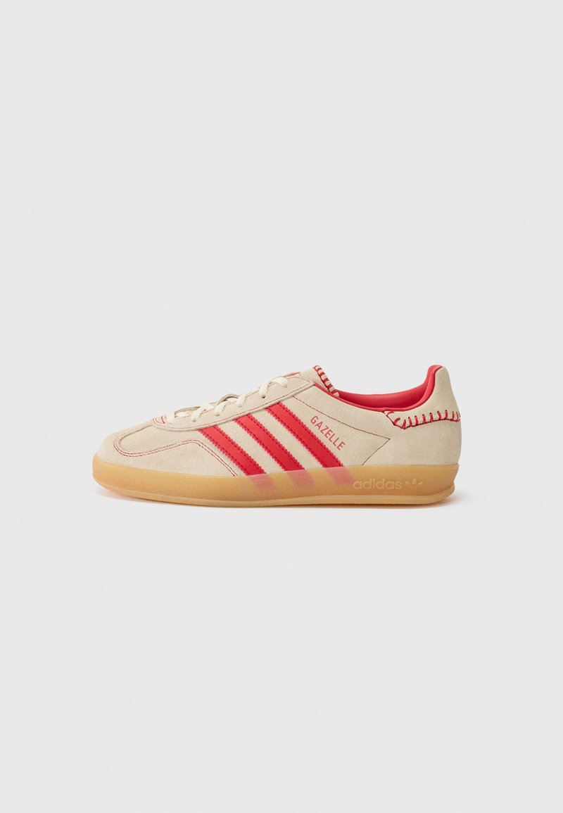 Baskets en daim beige avec des rayures et des accents rouges. Dotées d'une semelle en caoutchouc et de détails cousus. Nom du modèle "Gazelle" sur le côté.