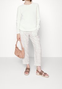 Pull en tricot blanc, pantalon à motif feuilles de palmier clair, sandales à bride marron et sac à main beige doux avec un design froncé.