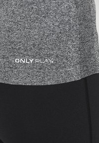 Szary top na ramiączkach z teksturowanej tkaniny, z czarną dolną sekcją, posiada biały logo "ONLY PLAY" w pobliżu talii, co stanowi kontrastujący detal.