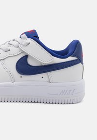 White leather sneaker with a blue leather swoosh, blue accents, and red branding on the tongue. Features a textured white rubber sole.