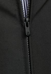 Svart zip-jacka med en smidig tygstruktur och ett kontrasterande randigt foder. Dragkedjan har en geometrisk logodetalj.