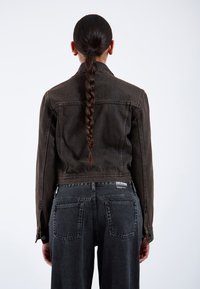 Giacca di denim marrone con cuciture a contrasto, design cropped e bottoni in metallo, abbinata a jeans neri a vita alta con tasche posteriori.