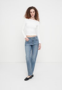 Λευκό μακρυμάνικο τοπ, ανοιχτό μπλε τζιν κανονικής γραμμής και μαύρα επίπεδα παπούτσια. Το ντύσιμο έχει casual εμφάνιση με μινιμαλιστικά στοιχεία σχεδιασμού.