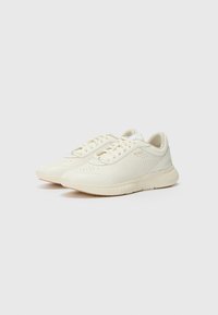 Lyse beige sneakers med strukturert overdel, rund tå, flat såle og snøring. Har subtile merking på siden.