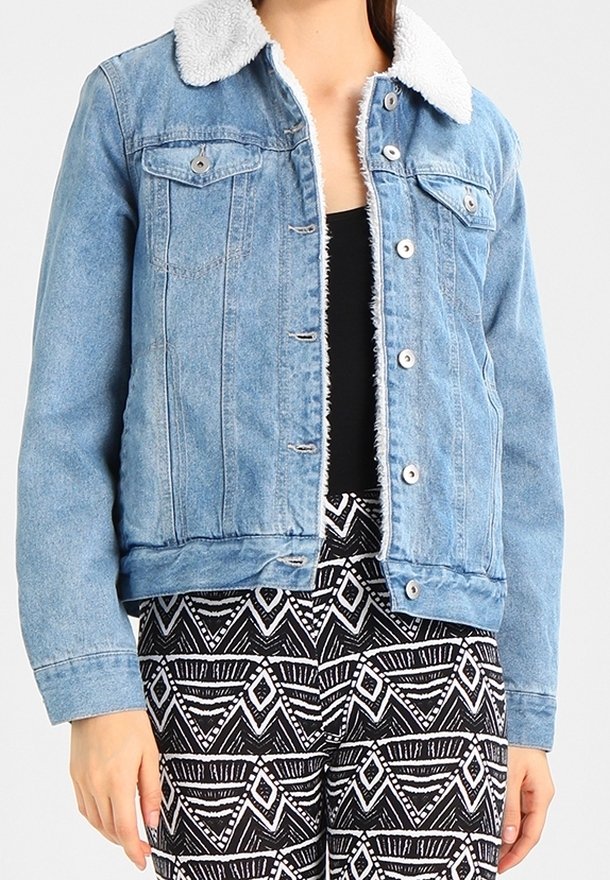 Giacca di jeans azzurro chiaro con colletto bianco e peloso, tasche frontali e bottoni metallici, abbinata a pantaloni a fantasia bianco e nero.