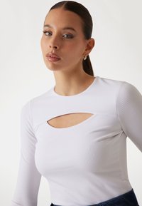White ribbed long-sleeve top featuring a round neckline and a keyhole cutout detail on the front, with a fitted silhouette.