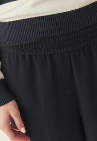 Pantalon de jogging décontracté bleu marine avec une ceinture élastique côtelée. Tissu lisse avec une poche latérale et des détails de poignets en tricot texturé.