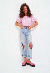 Top scurt din gingham roz cu mâneci puff, blugi deschiși la culoare cu rupturi mari la genunchi și sandale cu talpă înaltă și bretele roz.