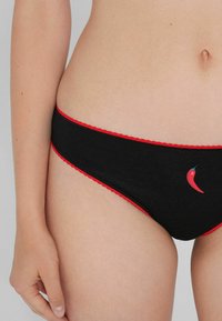 Culotte en coton noir avec une ceinture et des détails en rouge à bords festonnés, présentant un petit motif de piment rouge sur le côté gauche.