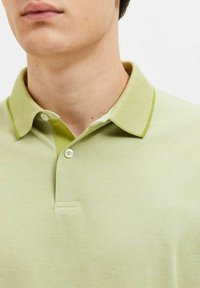 Polo de color verde claro con un cuello texturizado en verde más oscuro, cuenta con una tapeta de dos botones y un patrón sutil en toda la tela.