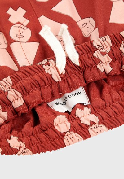 Červená látka so zberaným pásom, so hravým ružovým vzorom abstraktných postáv. Obsahuje biele šnúrky a štítok.