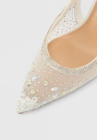 Beige stilet højdehæl med spids tå, mesh-overflade og prydet med flerfarvede rhinsten og små nitter langs foran og siderne.