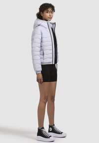 Light lavender puffer jacket with a hood, featuring quilted design and black zipper. Paired with black shorts and black high-top sneakers.
