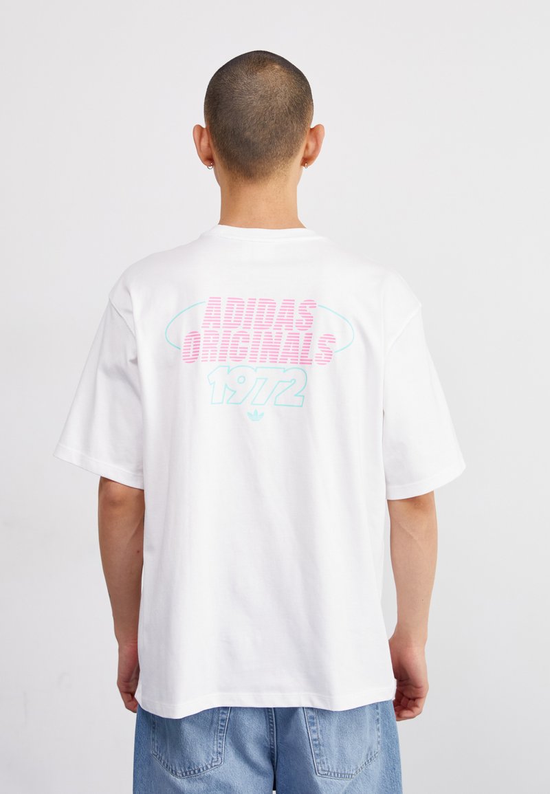Balta medvilninė marškinėliai trumpomis rankovėmis. Nugaros pusėje yra tekstas "ADIDAS ORIGINALS 1972" rožine ir mėlyna spalvomis, išdėstytu sluoksniais su kreiviu pabrėžimu.