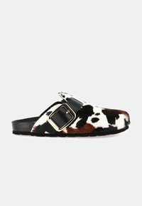 Sandalo a ciabatta in pelliccia sintetica con motivo a macchie di mucca in nero, bianco e marrone, con cinturino in pelle nera e fibbia metallica come dettaglio.