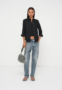 Melna pogu priekšā krekls, melns tops, gaiši zilas nodilušas džinsa bikses un sandales ar siksniņām. Pelēka teksturēta soma ar unikālu metāla detaļu.