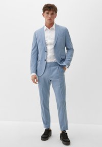 Blaues strukturiertes Anzug mit einem taillierten Blazer und schmal geschnittenen Hosen, kombiniert mit einem weißen Hemd und schwarzen Sneakers. Zwei-Knopf-Verschluss, seitliche Taschen.