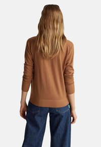 Bruine gebreide trui met een relaxte pasvorm, lange mouwen, geribbelde manchetten en zoom, gecombineerd met donkerblauwe brede jeans.