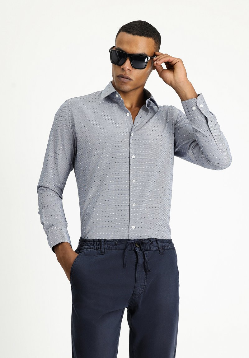 Camicia a maniche lunghe con motivo blu e punte bianche, colletto button-down, abbinata a pantaloni navy con coulisse.