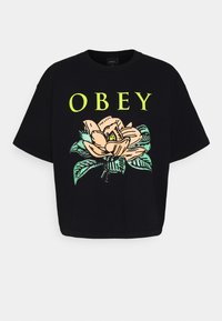 Černé tričko s krátkým rukávem, na kterém se nachází velká květinová grafika v pastelových barvách a výrazný nápis "OBEY" v neonově žluté.