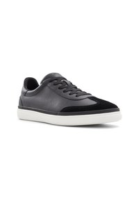 Zapatilla de cuero negra con una puntera de ante negro texturizado, suela de goma blanca y cordones planos. Forma redondeada con un acabado suave.