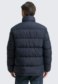 Navy zilā pūkainā jaka ar kvadrātveida dizainu, augstu apkakli un sānu kabatām. Izgatavota no viegla, teksturēta auduma.