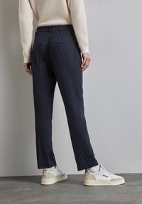Marineblauwe pinstriped broeken met een getailleerde pasvorm, voorzien van twee achterzakken en gecombineerd met witte en beige sneakers. De textuur is glad.