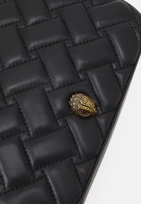 Črna usnjena torba z tkanim vzorcem, ki ima zlat ton sklo s stiliziranim pticama in okraski.