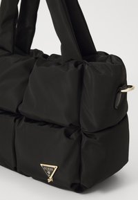 Black nylon handbag with a puffy design, featuring a gold triangular logo tag, double handles, and soft, textured surface.