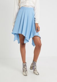 Falda asimétrica plisada de color azul claro con una textura suave, llevada sobre botas de tobillo con estampado de serpiente, con un acabado texturizado y tacón angulado.