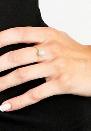 Gouden ring met een gladde, witte parel in het midden. Het ontwerp heeft een eenvoudige, dunne band met een minimalistische esthetiek.