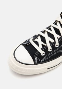 Sorte lerretssneakers med hvite snører, gummitåhette og kontrasterende sømmer. Teksturert stoff med lavprofildesign.